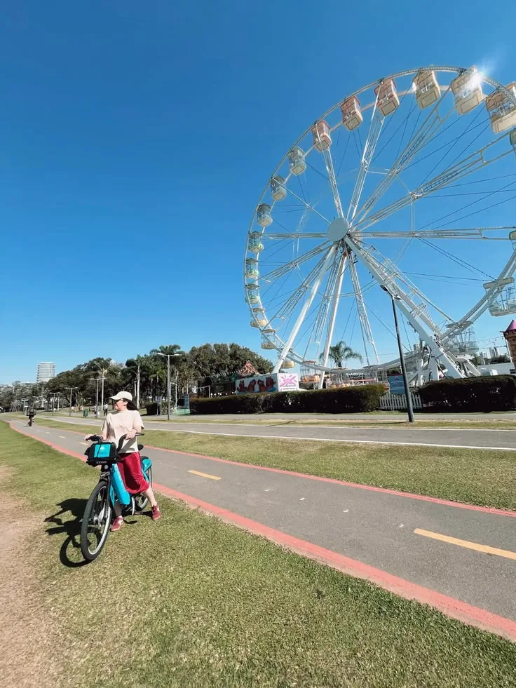 Pessoa com bicicleta diante de roda-gigante instalada no Parque Barigui durante evento