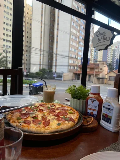 Pizza e bebida sobre a mesa junto à janela da Casa de Tia