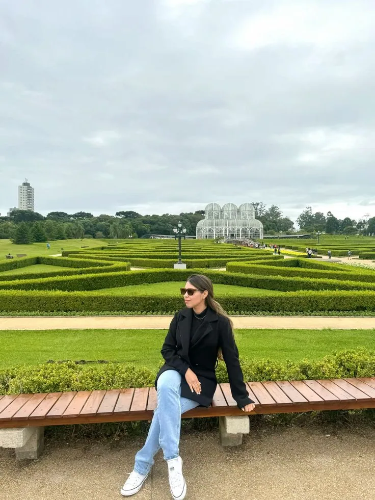 Pessoa sentada em banco com o jardim e a estufa ao fundo