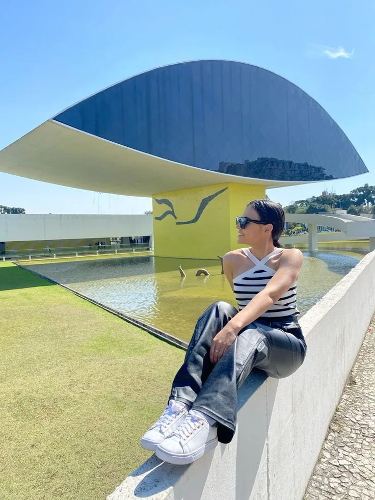 Pessoa sentada na passarela diante do edifício do Olho